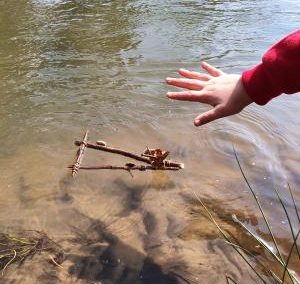 a little trianfular boat make from 3 twigs floating in a stream