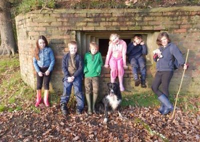 6 children posing in front of a WW2 Pill box in the fields at Huckleberries with Jet the dog standing in front