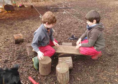 2 children sitting on either end of a make shift seasaw.